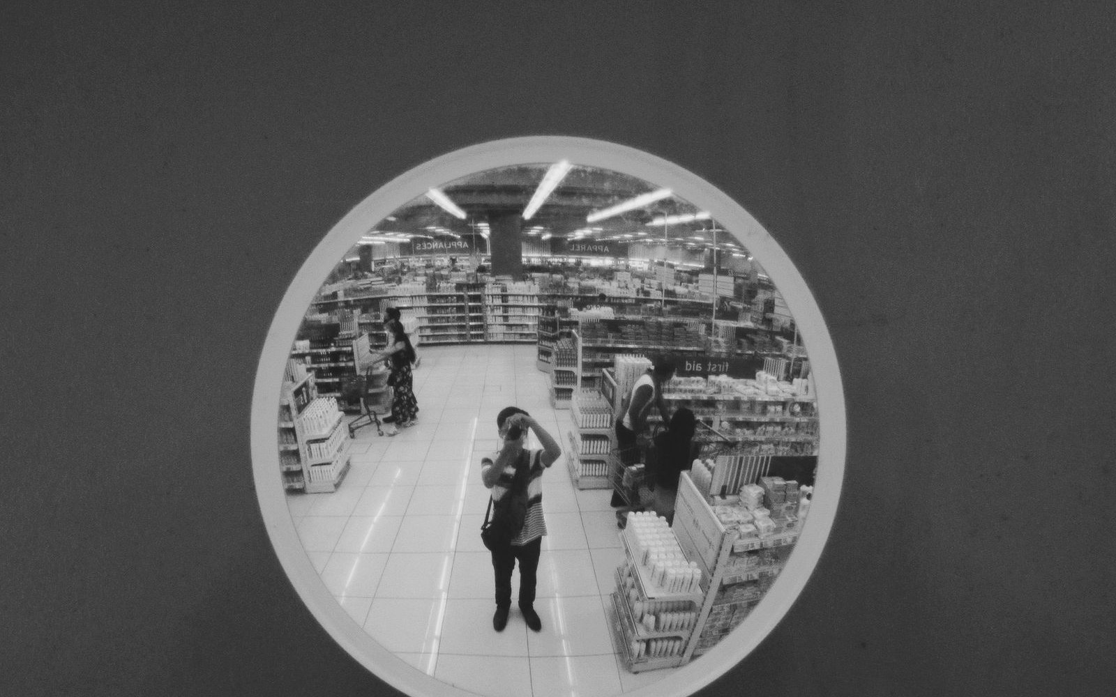 Shopper reflected in a round security mirror in a supermarket aisle